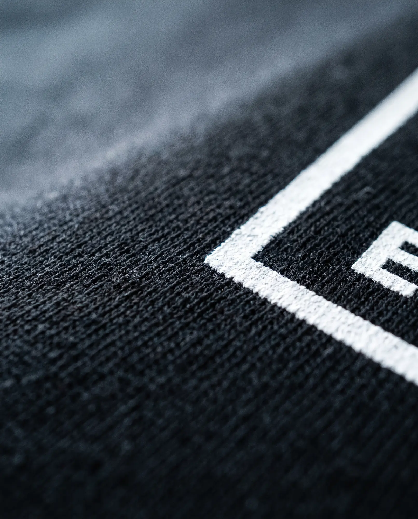 A macro photograph of the white plastisol print edge sitting on the black 215gsm weave.