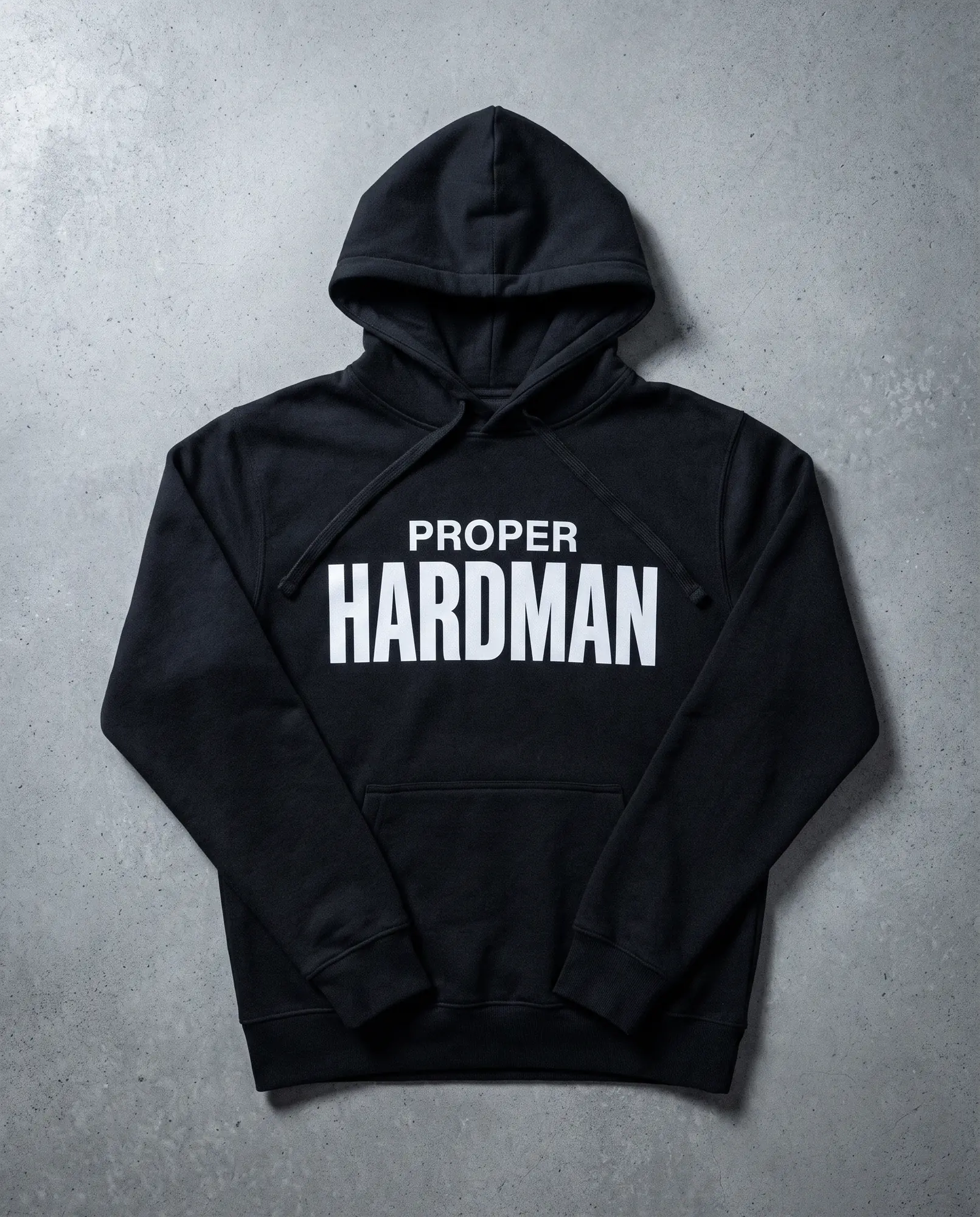 A heavyweight black hooded sweatshirt laid flat on grey concrete, PROPER HARDMAN screen printed across the chest in white.