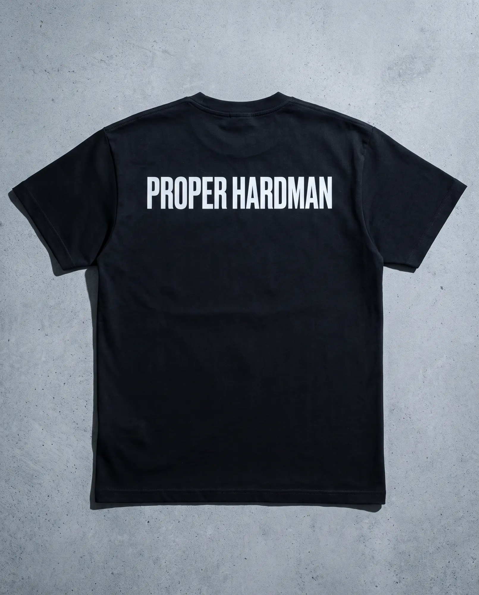 The reverse of the black t-shirt, plain, showing the shoulder seam and hem.