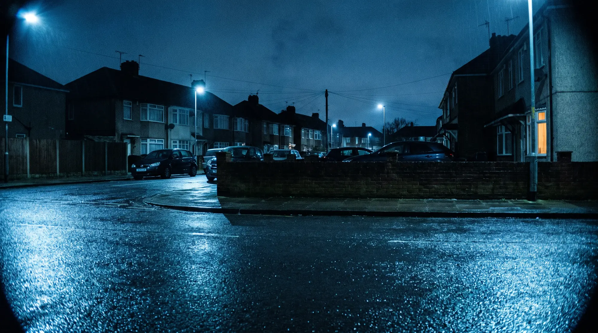 A wet residential street at night, terraced houses and street lamps reflected in the road